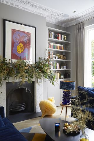 Living room with grey walls, bookcase in alcove and marble fireplace with foliage decorations one mantelpiece.