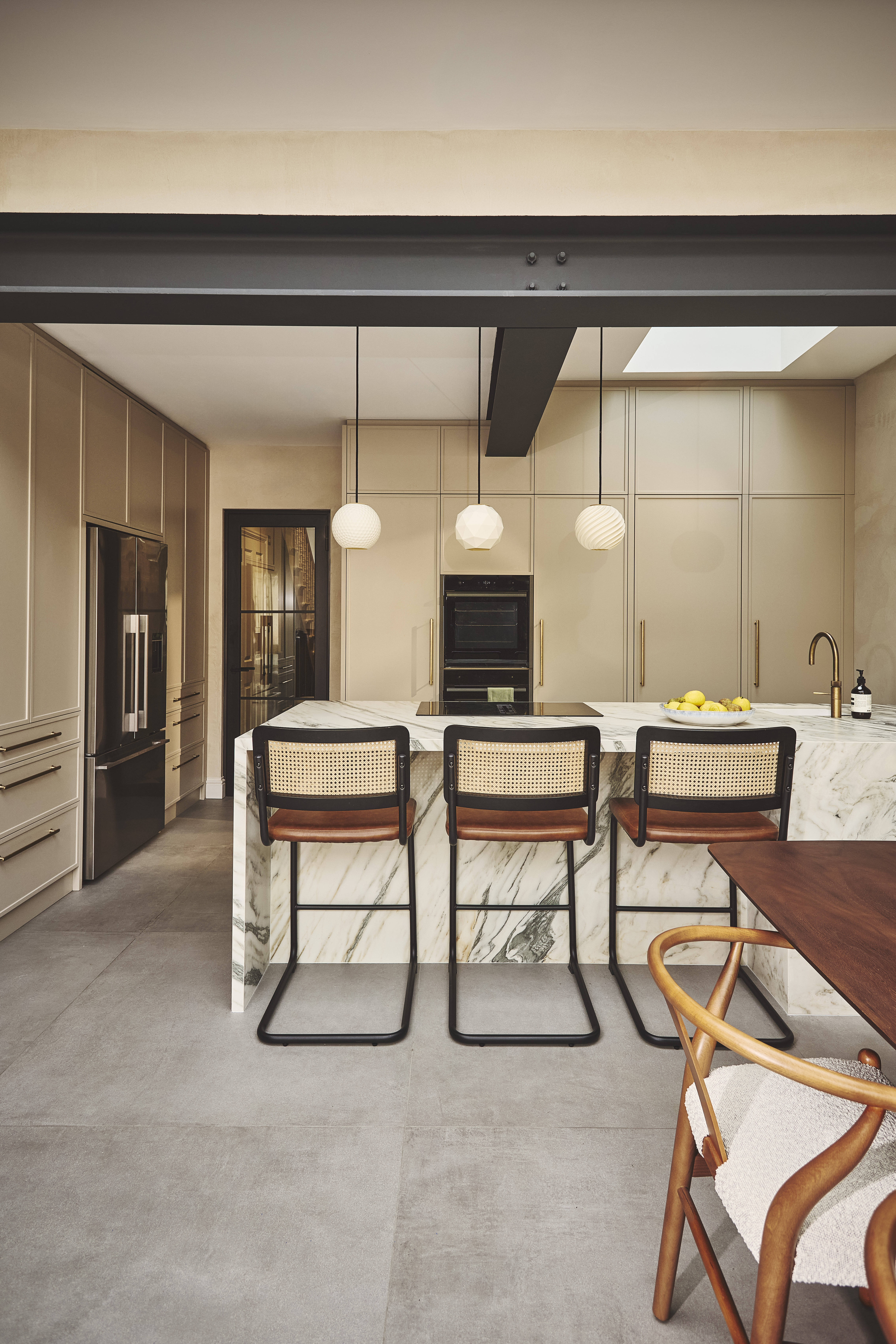 open plan kitchen in a warm, beige color with a central peninsula with bar seating and a banquette seating area off to the side