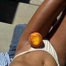 Woman sun-bathing with a bitten peach on her lap
