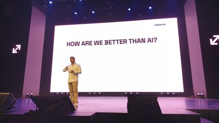 Joaqu&iacute;n Cuenca Abela of Freepik speaking at a conference in front of a slide reading "How are we better than AI?"
