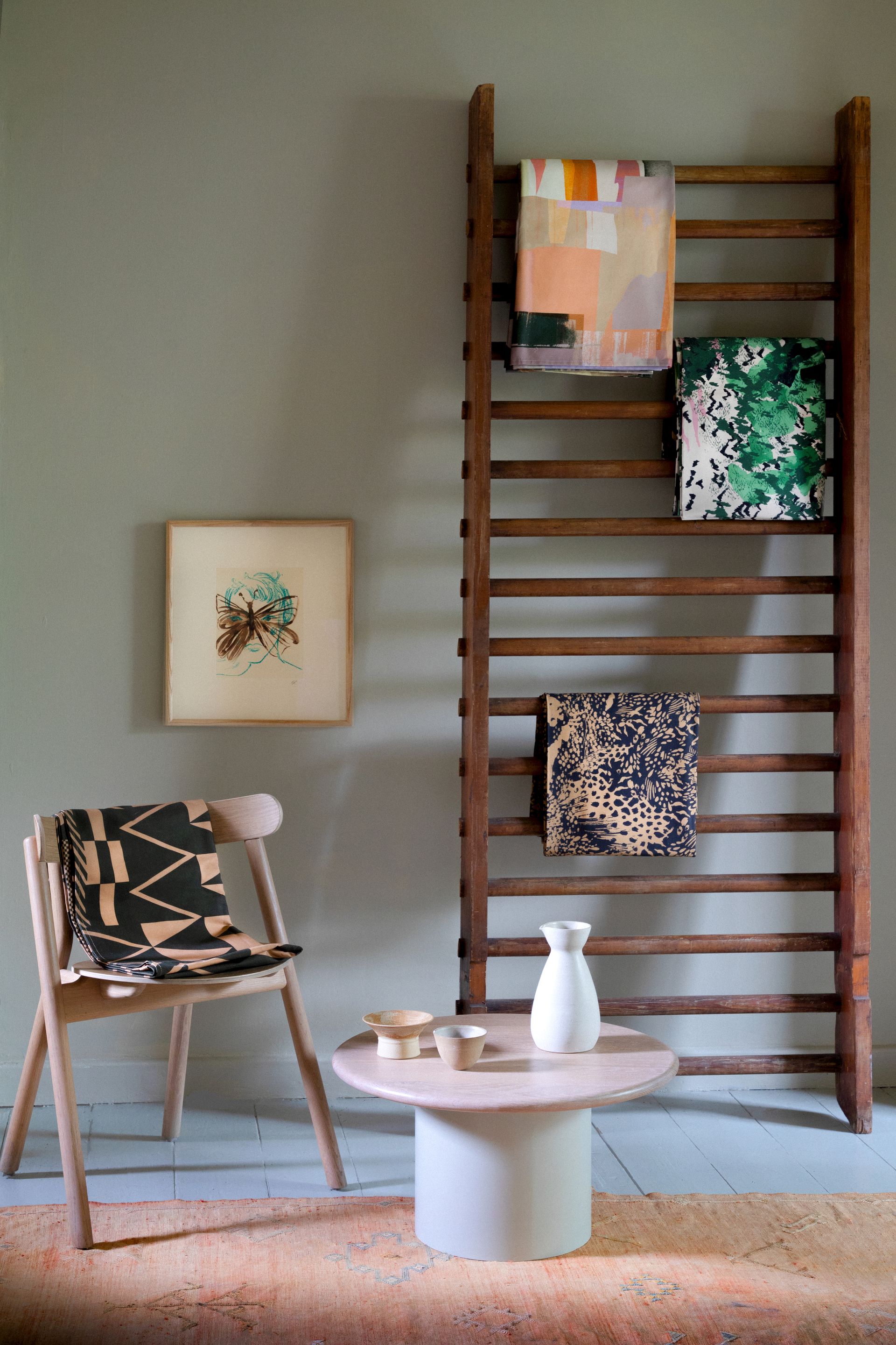 A living area with a low coffee table, a wooden chair, and a wooden gymnasium ladder holding textiles and cloths