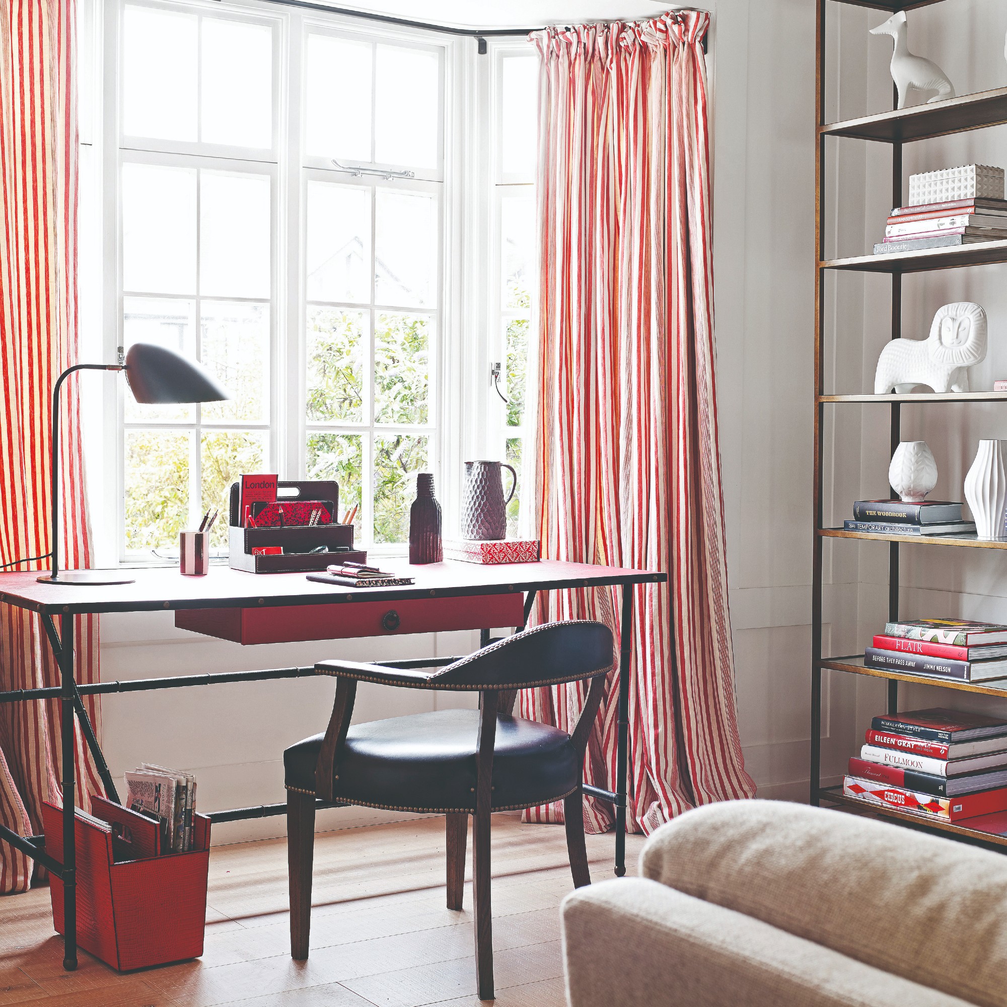 A home office with the desk positioned in a bay window dressed with striped curtains