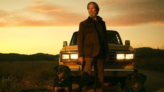 Jeff Bridges stands in front of a car with two dogs