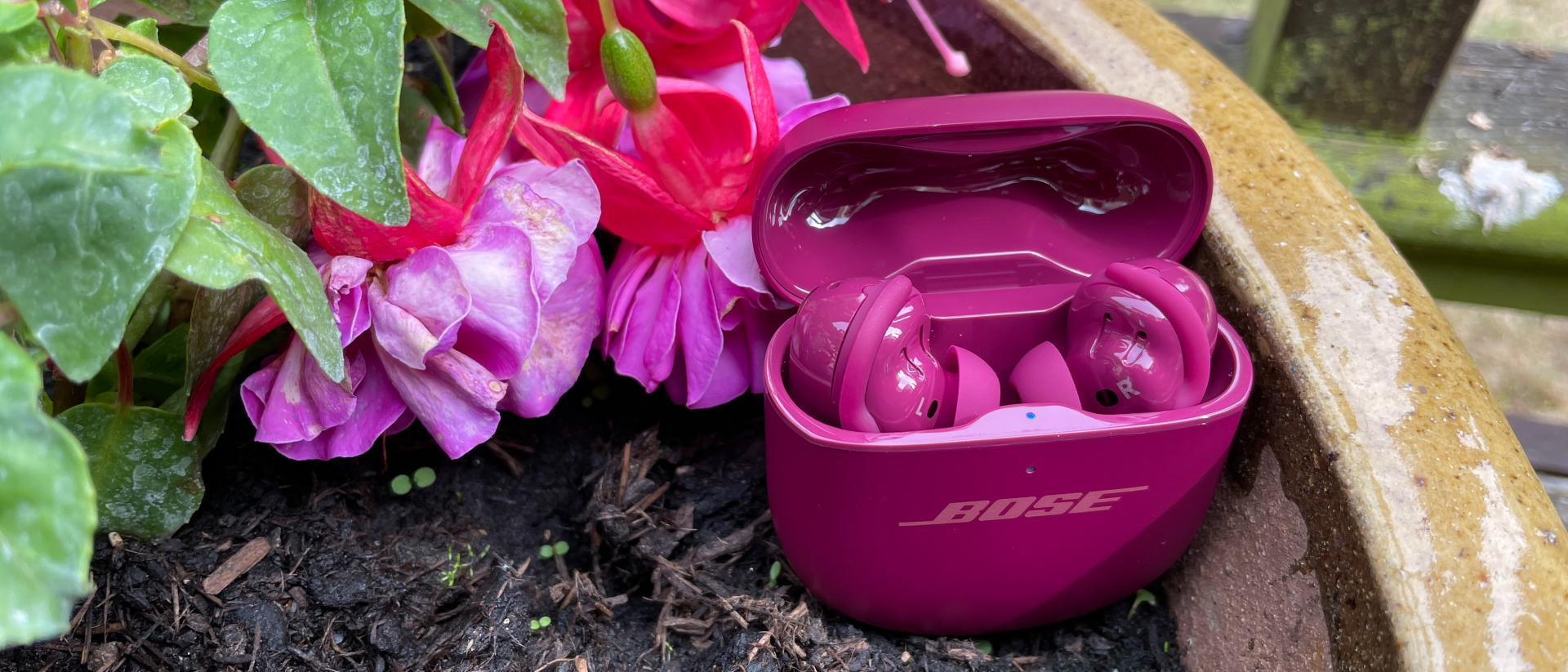 Bose QuietComfort Ultra Earbuds Gen 2 in a flower bed, next to purple flowers that are a similar color to the buds themselves 
