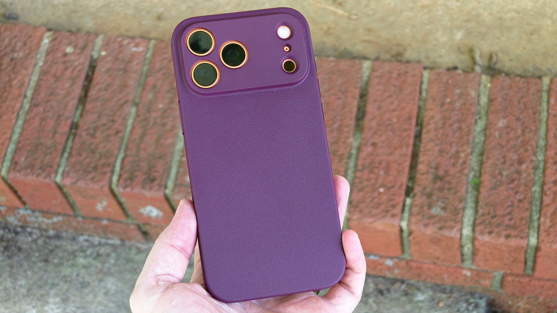A burgundy Dbrand MNML case on an orange Apple iPhone 17 Pro Max