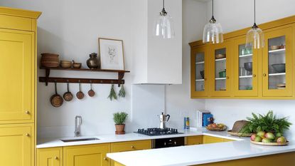 A small yellow kitchen with trio of glass pendants, shaker style cabinetry and white walls