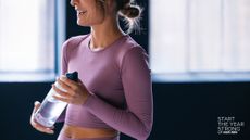 A woman in workout kit standing with a water bottle in the gym