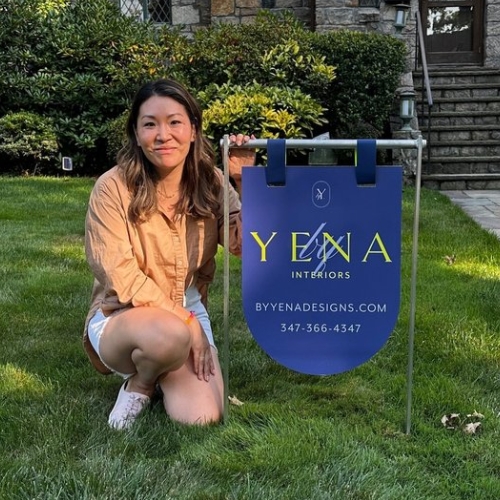 Image of a woman in an orange shirt in a yard next to a blue sign.