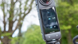 A photo of the Insta360 X4 mounted on handlebars with green foliage in the background. The rear touchscreen is on display and is showing a 4K/60p resolution selected in single lens mode.