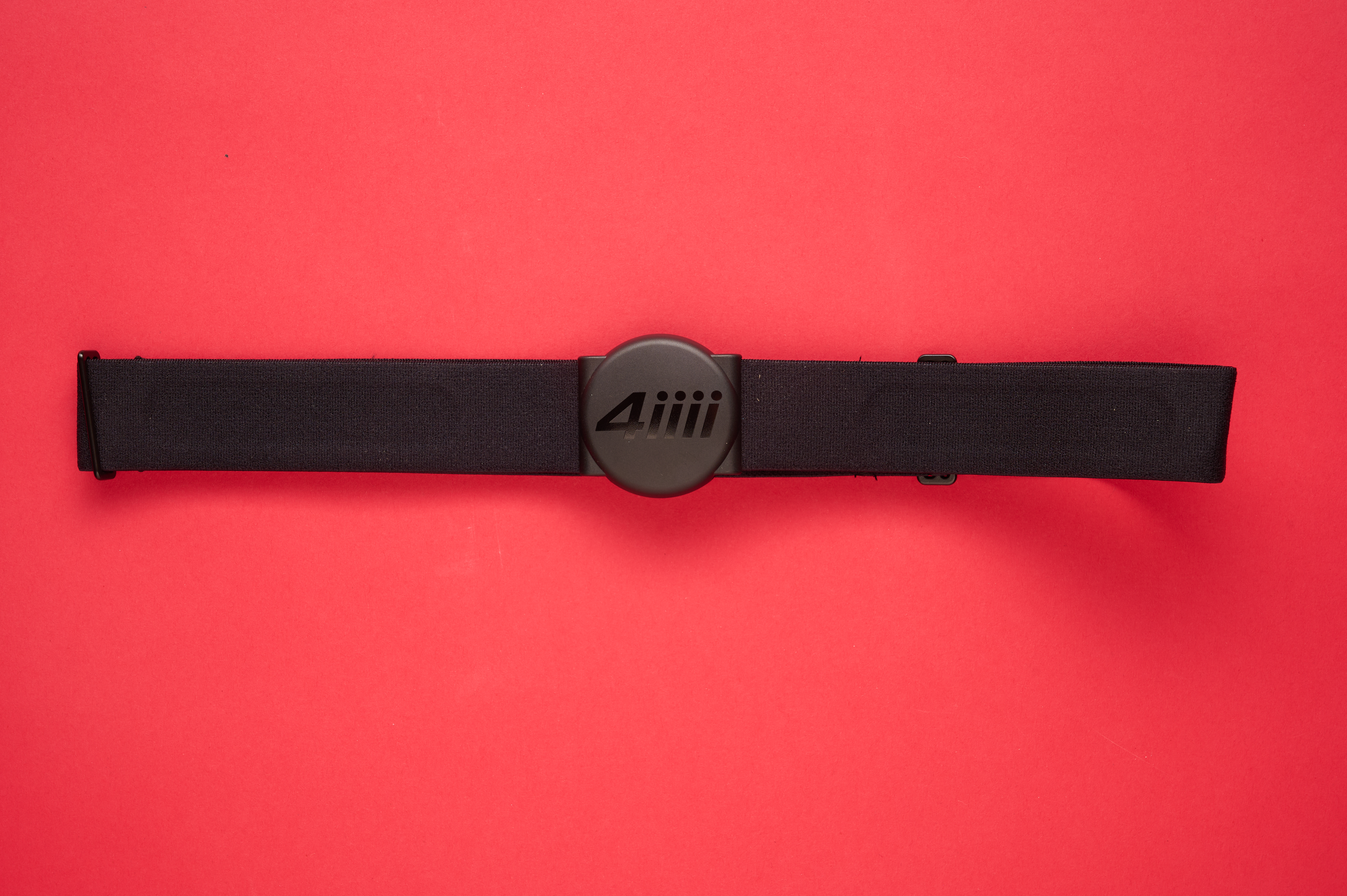 4iiii Viiiiva heart rate monitor with its rounded body, laid flat on a red background