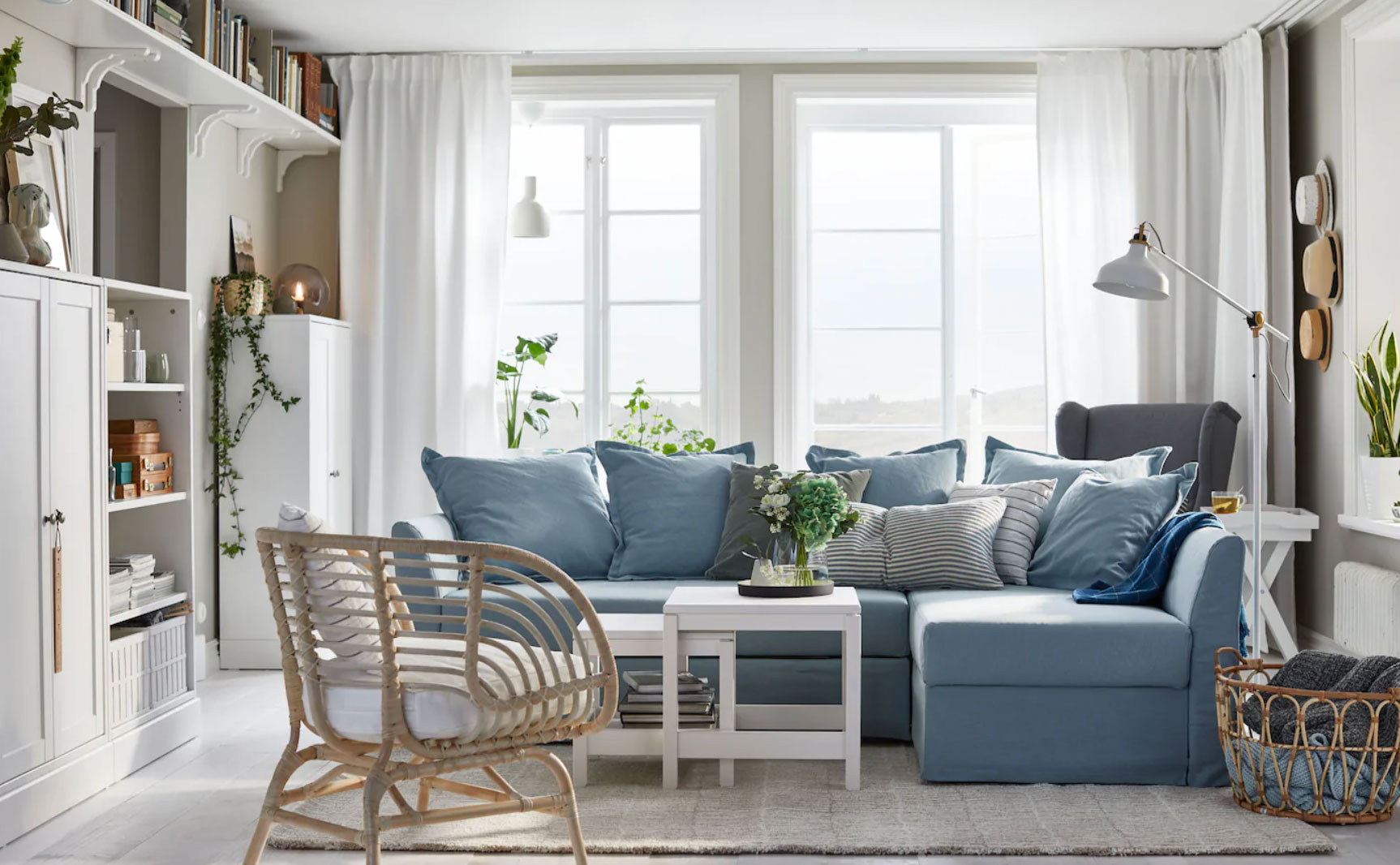 A grey living room with blue L-shaped upholstered sofa, rattan chair and white wall lamp.