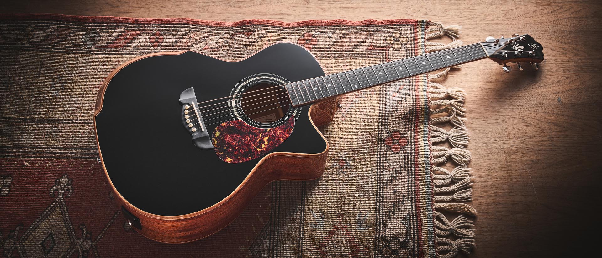 Harley Benton CLG-650SM-CE Black: the handsome but affordable cutaway acoustic isd photographed against a patterned rug on a wooden floor.