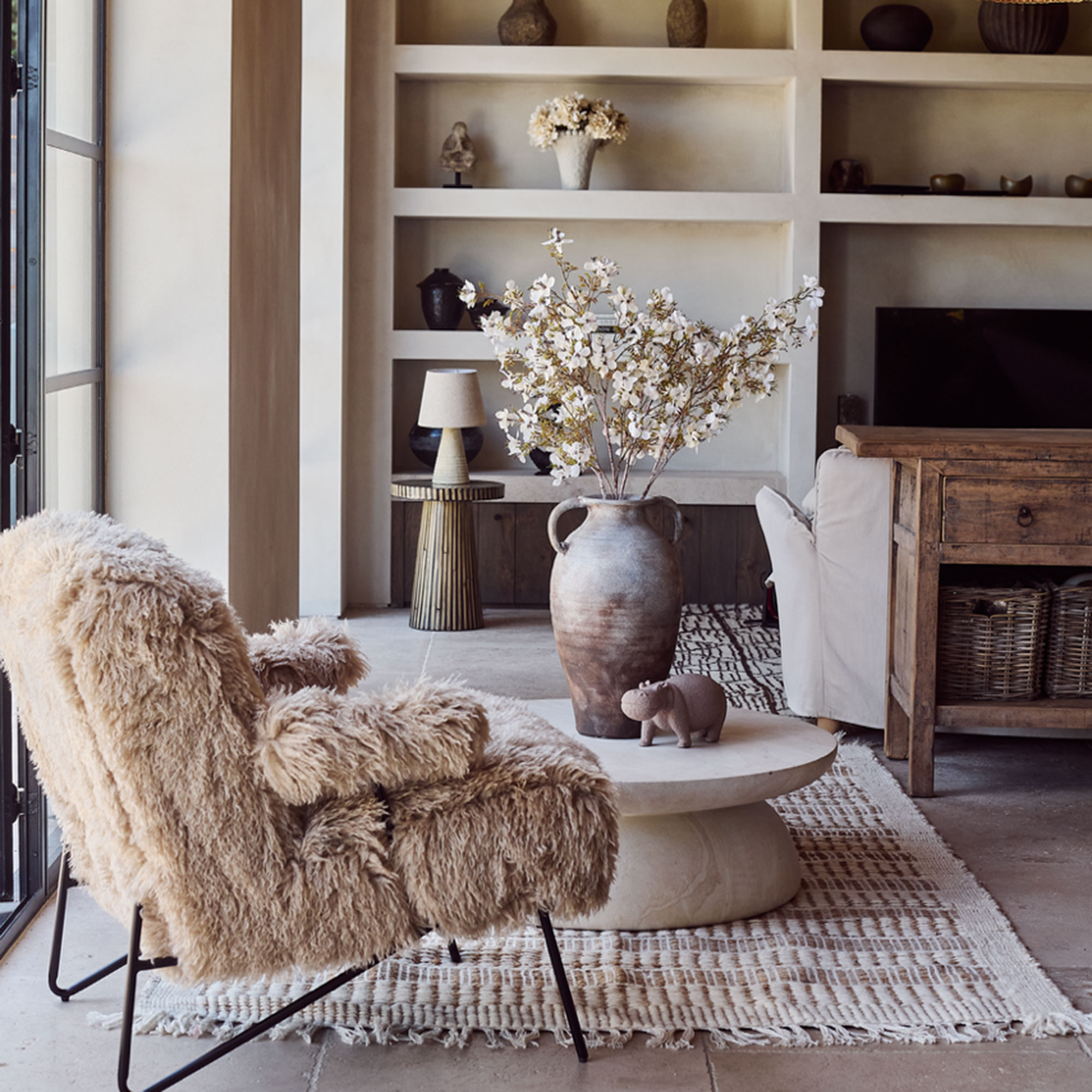 Neutral living room with fluffy armchair and stone coffee table and urn.