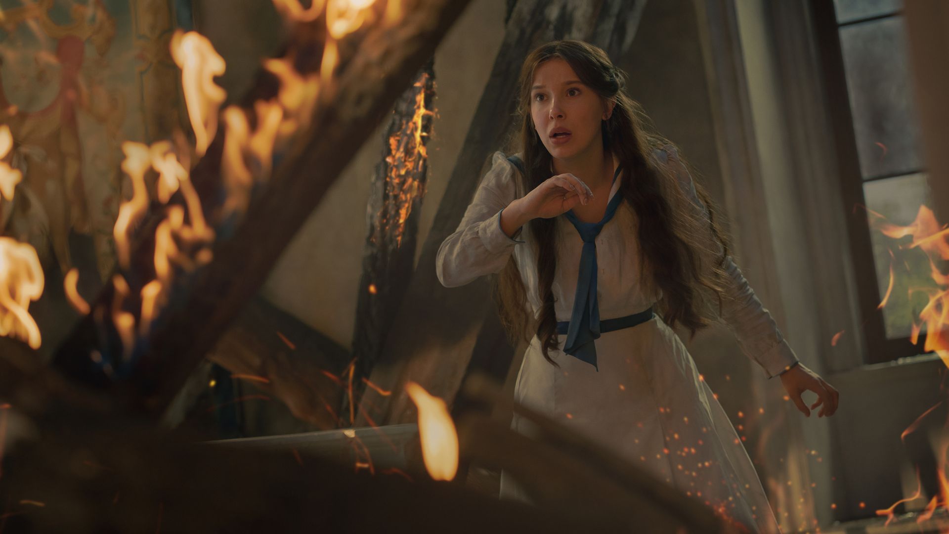 Millie Bobby Brown stands in a room on fire
