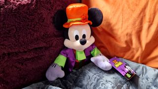 Halloween Mickey Mouse plush leaning up against two cushions, covered by a gray blanket