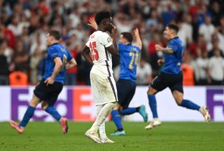 Bukayo Saka looks dejected after missing a penalty for England as Italy players celebrate victory in the final of Euro 2020.