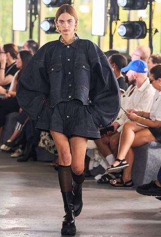 model's stylish outfit with socks, including a large jean jacket with matching shorts and knee-high sheer socks and chunky ankle boots