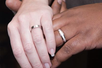 Interracial couple holding hands with wedding rings.