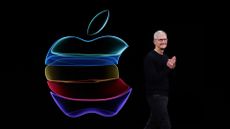 Tim Cook presenting during an Apple keynote, on black background, with multicoloured Apple logo beside him