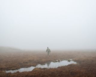 a man walking in brown field and fog