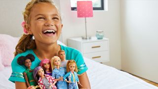 A young girl holding a range of Barbie dolls.