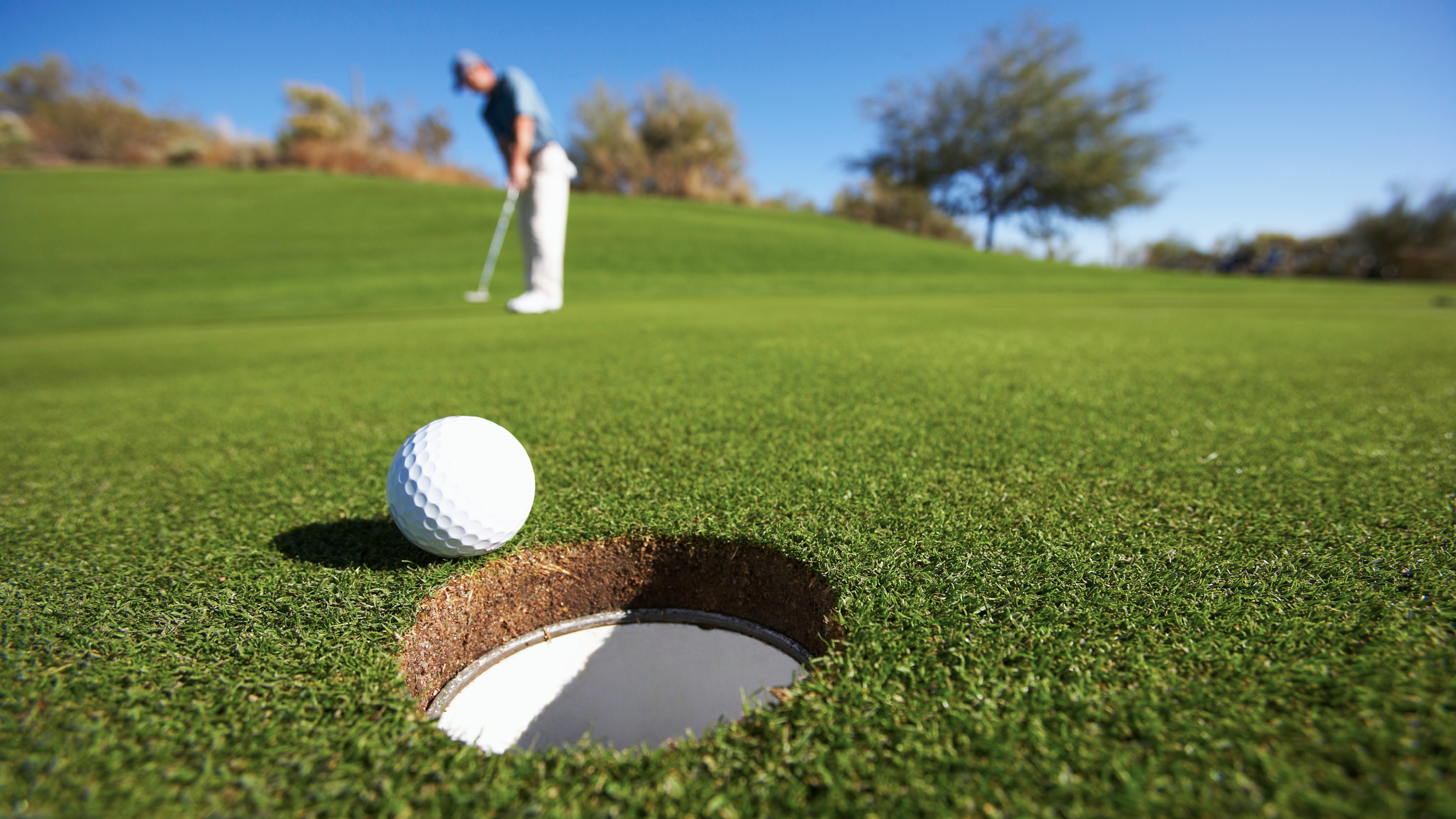 Image of a player standing over a putt with the ball rolling into the hole