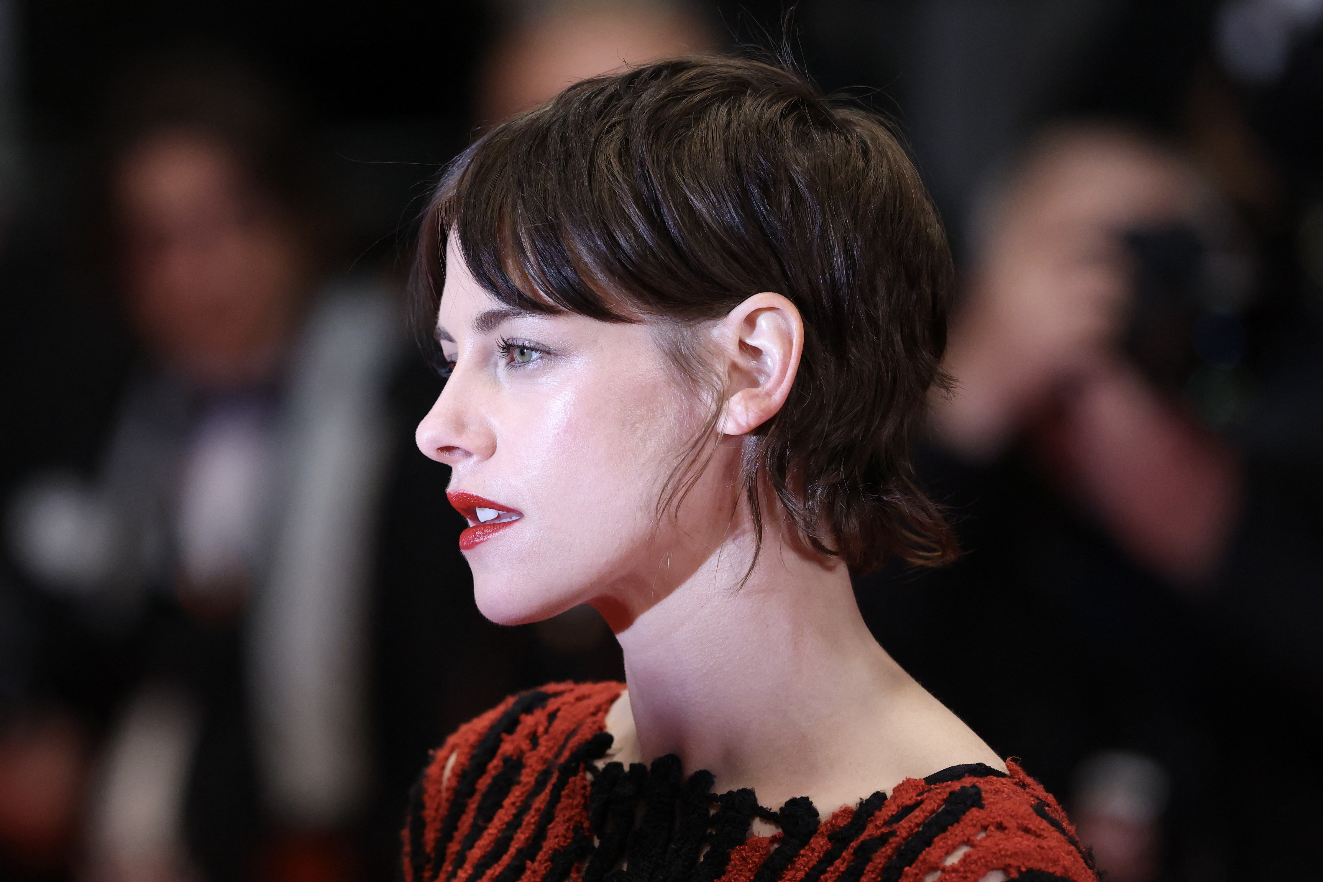 a woman with short, brown hair poses for paparazzi photos on a red carpet at a film festival