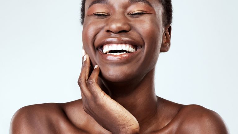 Skincare for sensitive skin: woman with glowing skin touching her face and smiling