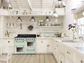 white kitchen with loww hanging lights and mint green/blue stove by smeg