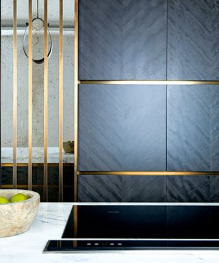 A black kitchen idea with black wooden panel with bronze accents and white worktop