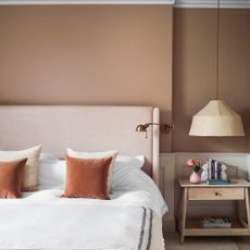 A bedroom with plaster pink walls and a bed with a cream headboard