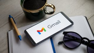 Gmail branding and logo displayed on a smartphone screen sitting on a desk.