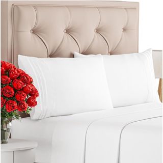 White bed sheets on a beige colored bed with a vase of roses