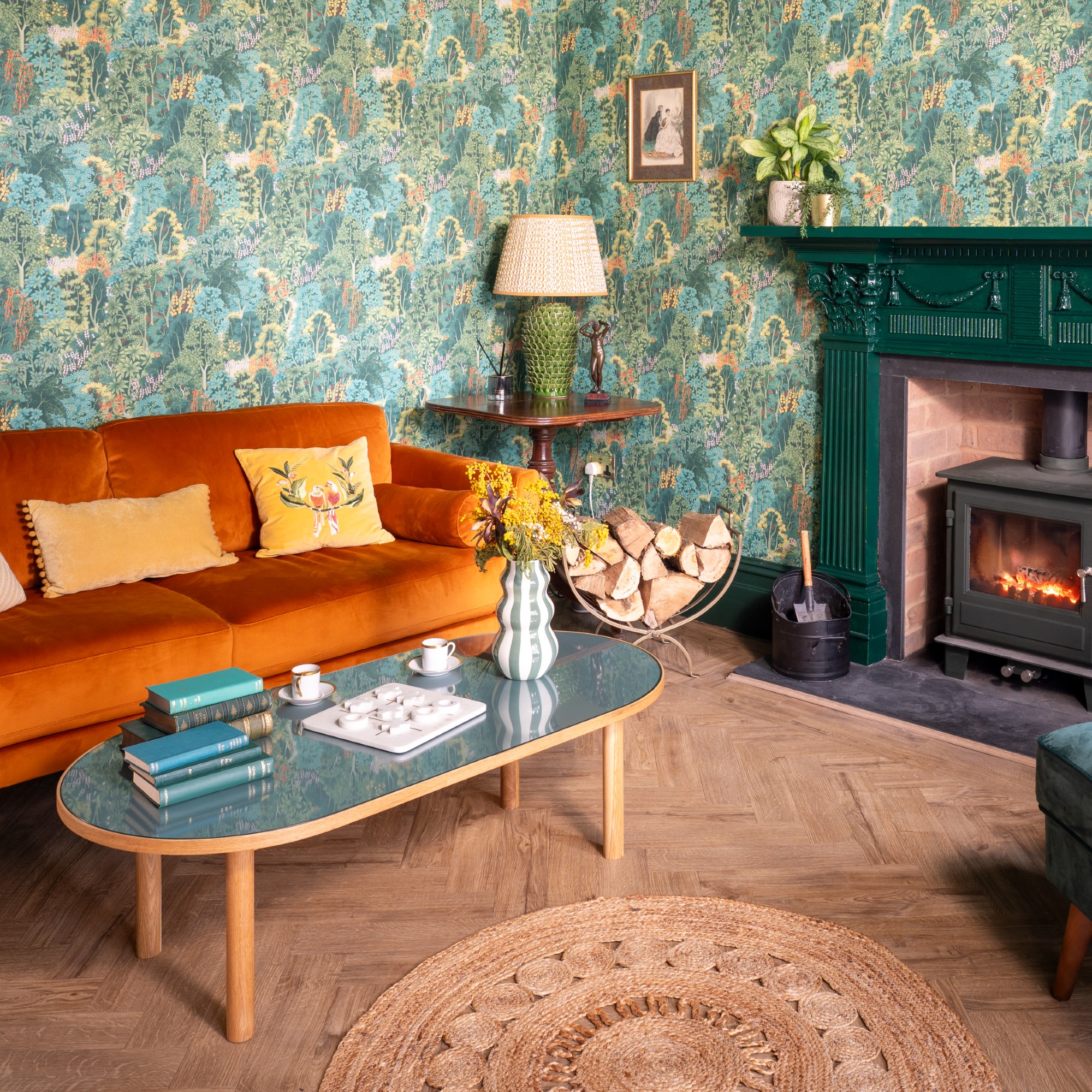 A wallpaper-covered livig room with an orange velvet sofa and a green-painted fireplace