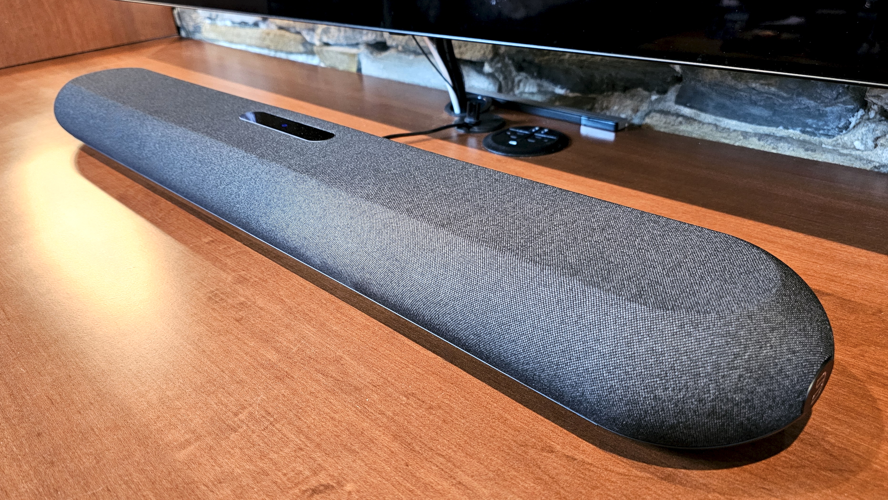 The Bluesound Pulse Mini soundbar pictured on a wooden surface below a TV