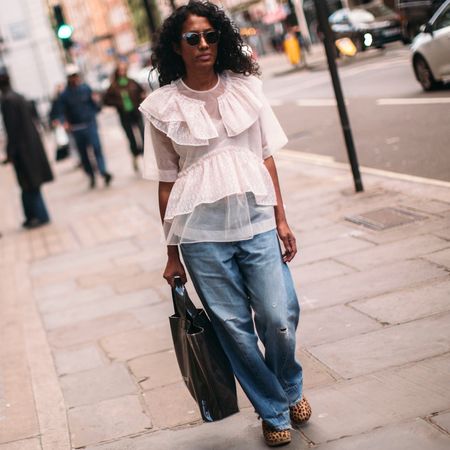 A fashion week attendee wearings sunglasses, white blouse, and jeans