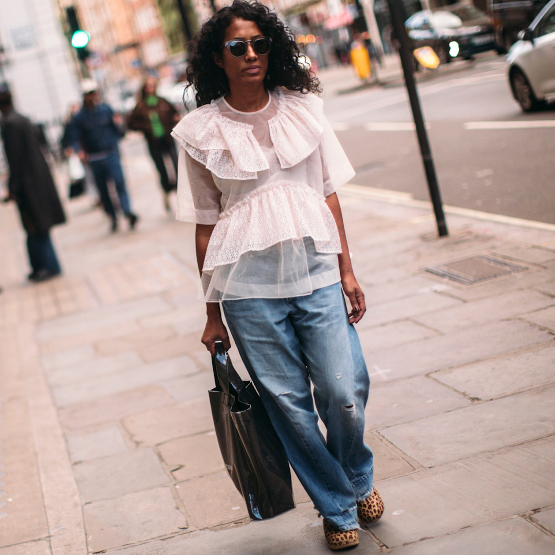 A fashion week attendee wearings sunglasses, white blouse, and jeans