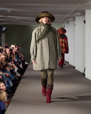 a model walks the runway at Copenhagen Fashion Week wearing a button up jacket with boots made with upcycled Chanel tweed