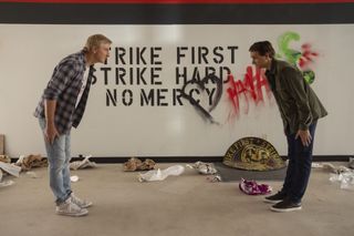 William Zabka as Johnny Lawrence and Ralph Macchio as Daniel LaRusso bowing to each other in front of a sign at the cobra kai dojo