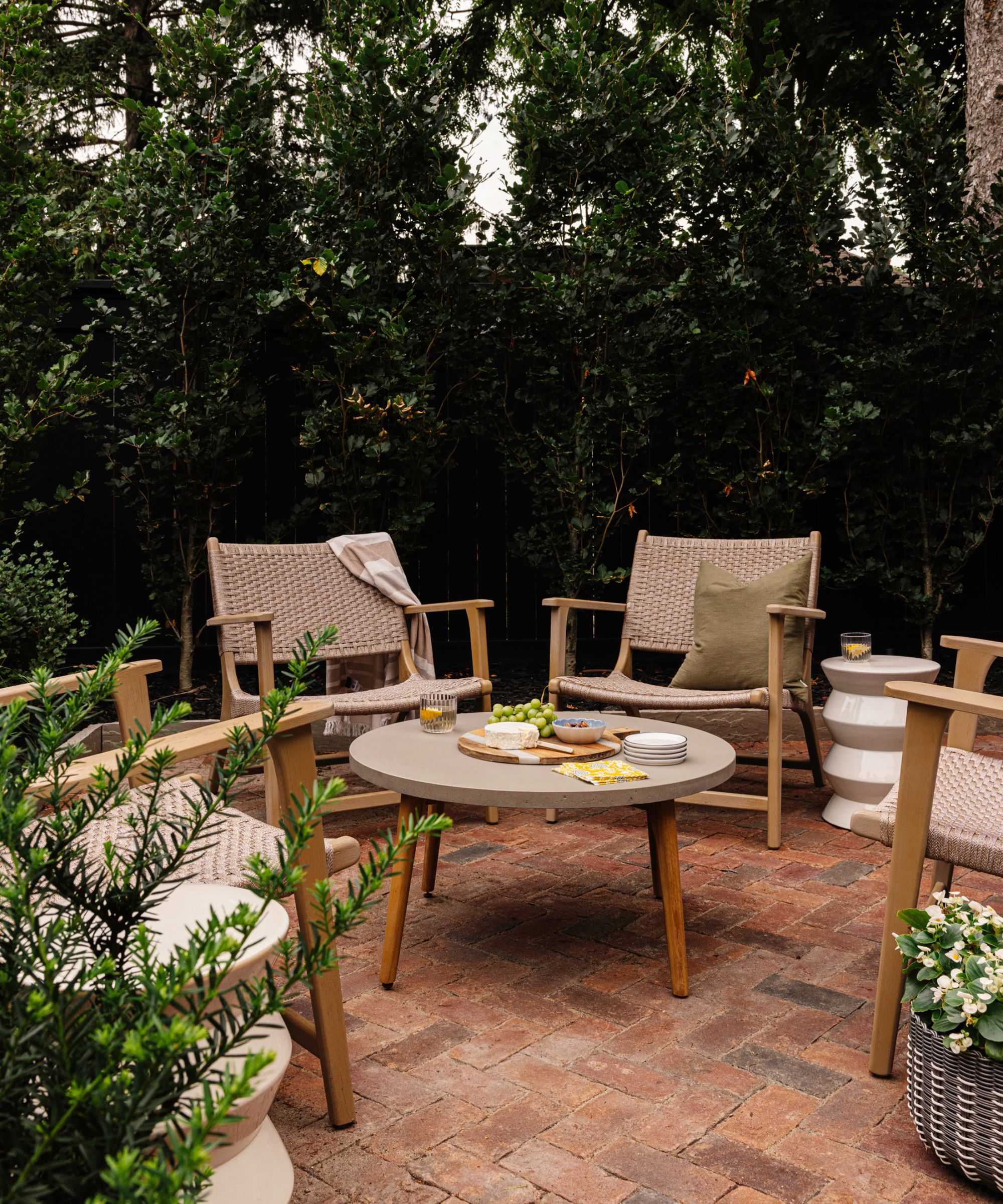 Low-slung outdoor armchairs around a circular table on a paved terrace surrounded by trees