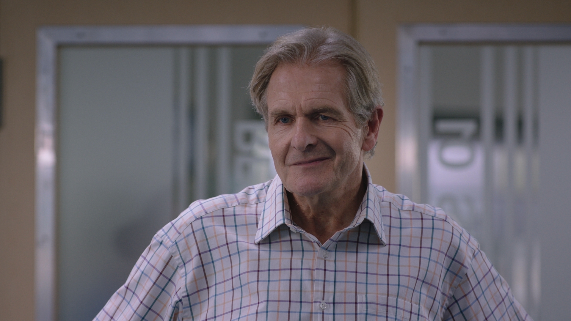Russell Whitelaw in the hospital, wearing a checked shirt and a snarling lob-sided grin.
