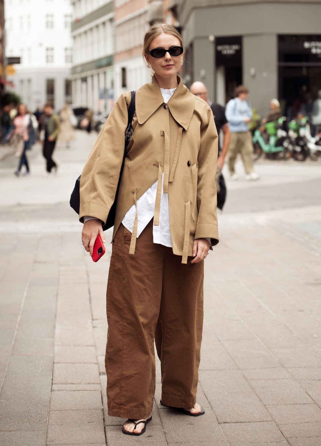 A guest wears white shirt, brown wide pants, beige jacket or a trench coat and a black bag outside Filippa K presentation during Copenhagen Fashion Week day four on August 07, 2025 in Copenhagen, Denmark.