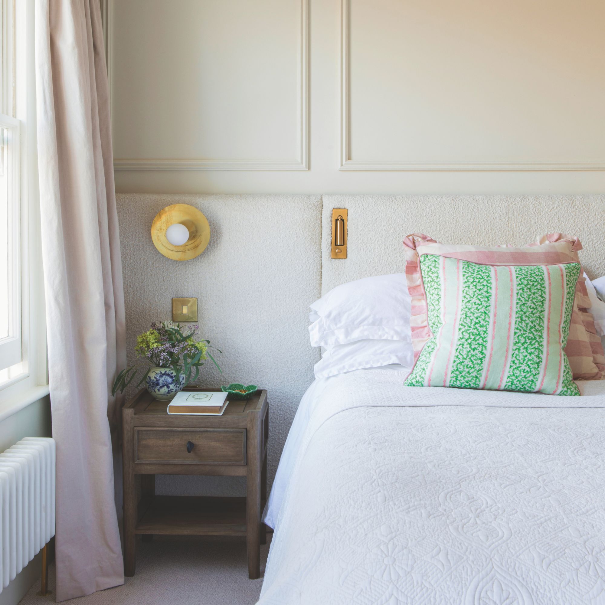 Neutral bedroom with panelling on the walls and white bedding on the bed, next to a wooden side table