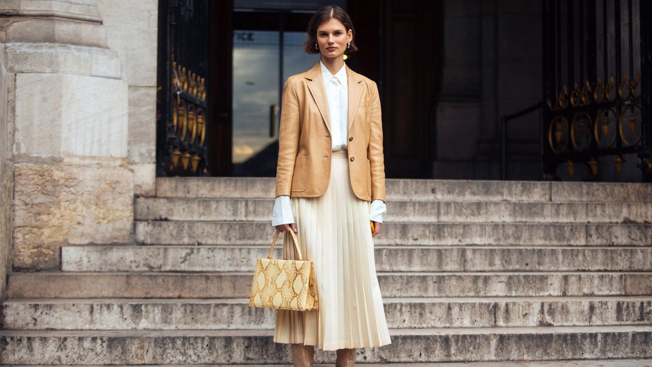 woman in white pleated skirt, blazer, and boots