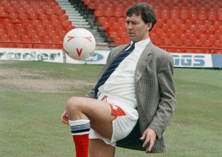 Bryan Robson, wearing a jacket, shirt and tie and football shorts and socks, does keepie-uppies on the pitch after being appointed as player-manager of Middlesbrough, March 1994