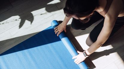 Hot pilates: A woman rolling out a workout mat