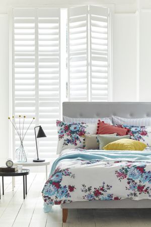White bedroom with white shutters and bright patterned bedding