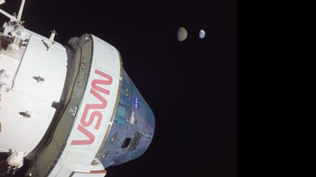 A large white space shuttle labeled in red "NASA" is seen in the darkness of space. 