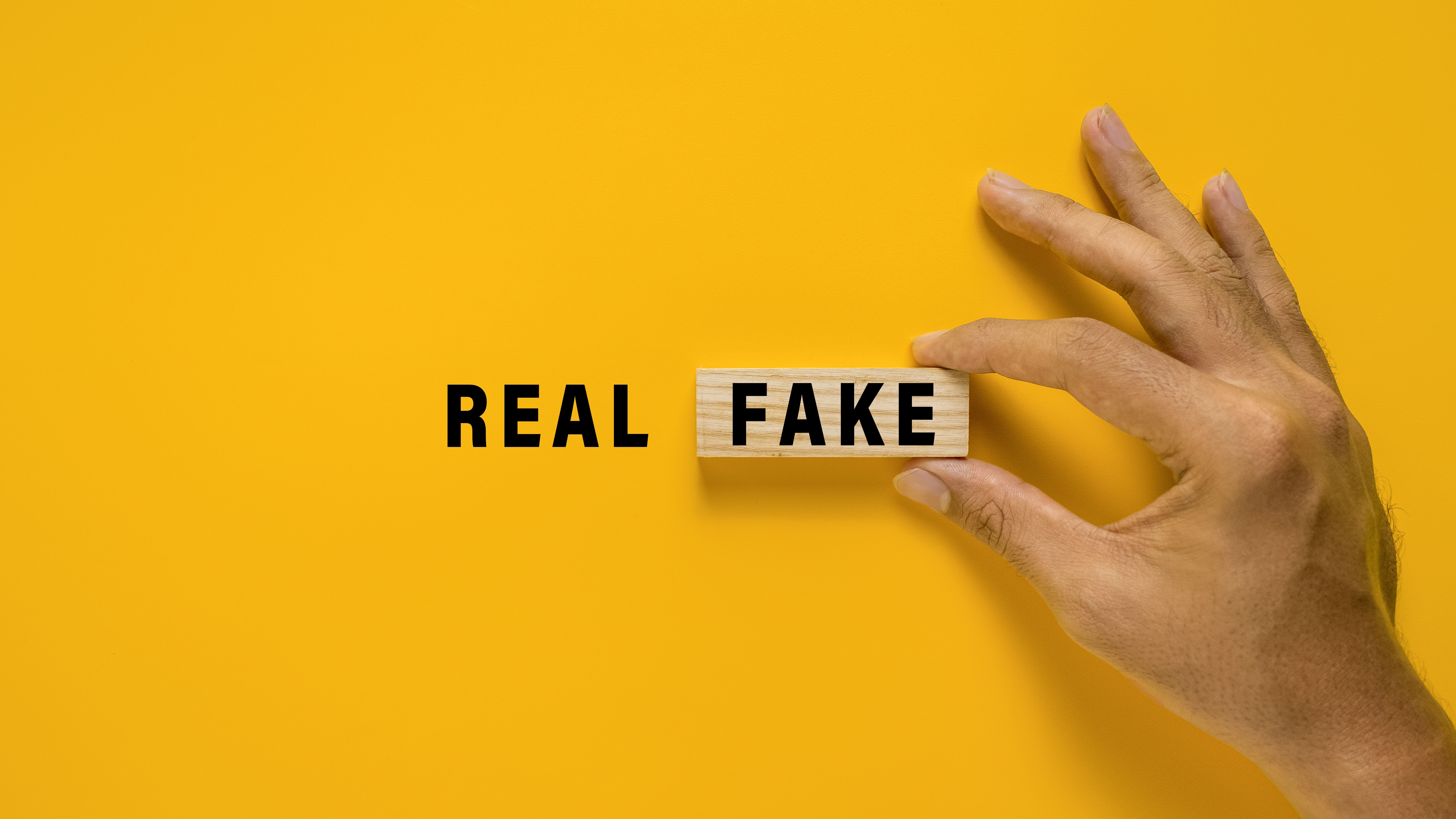 Male hand put wooden blocks with real and fake words text. isolated on yellow background