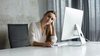 A frustrated office worker sitting on her desk in front of her monitor